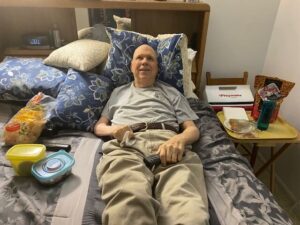 Bill lying in bed surrounded by food, smiling